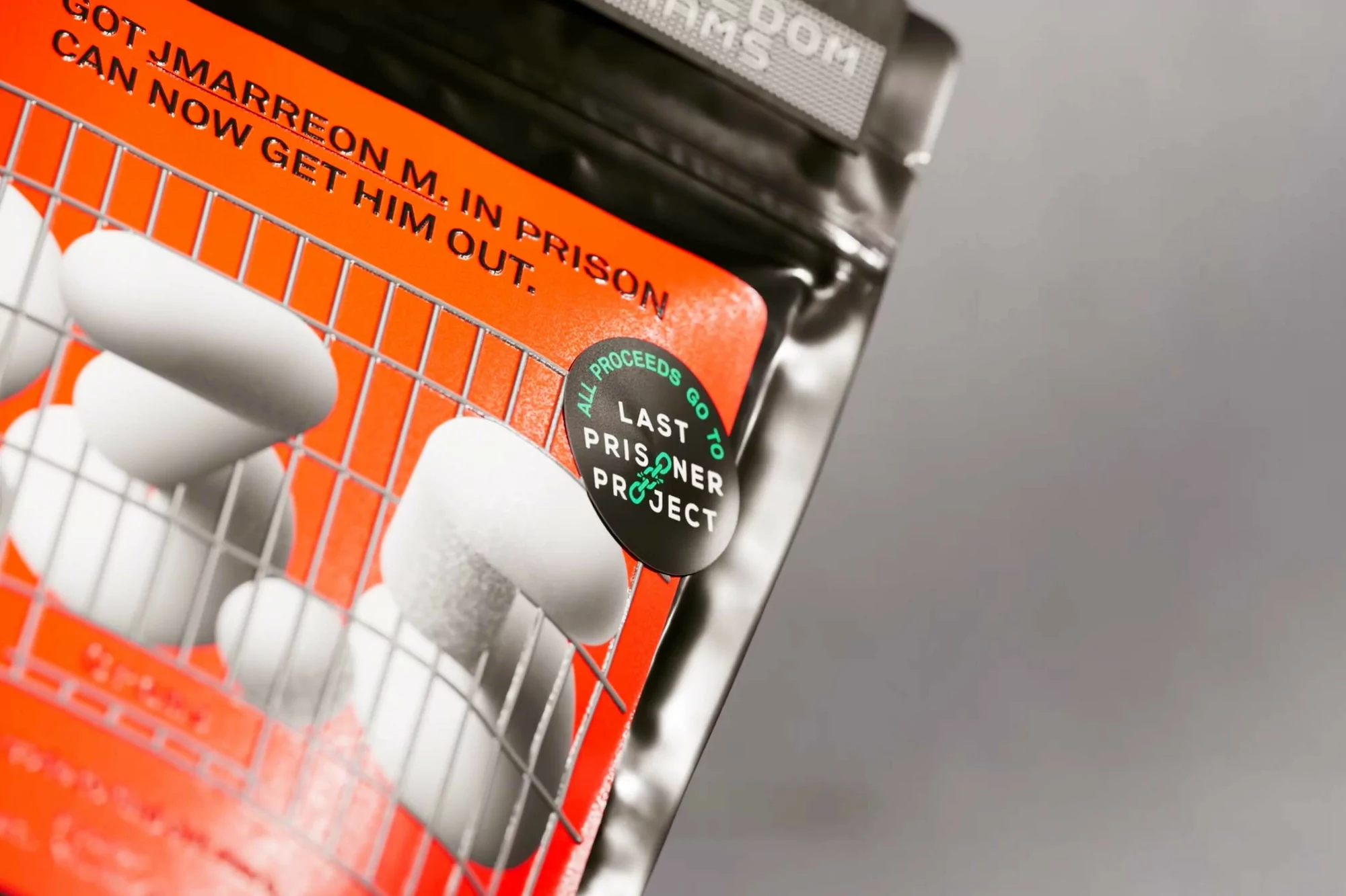 Close-up of a product package featuring white, oval objects behind a metal grate, with orange background, black text, and gray backdrop.