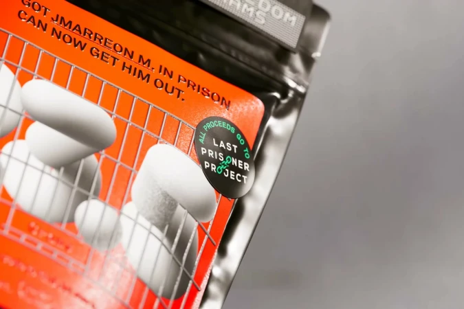 Close-up of a product package featuring white, oval objects behind a metal grate, with orange background, black text, and gray backdrop.