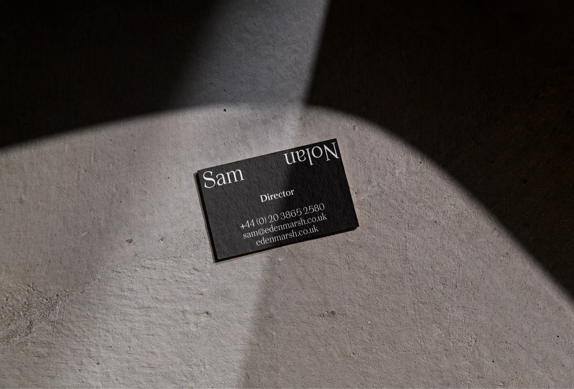 Close-up of a black business card with white text on a concrete surface with a light spot shining on it, minimalist design.