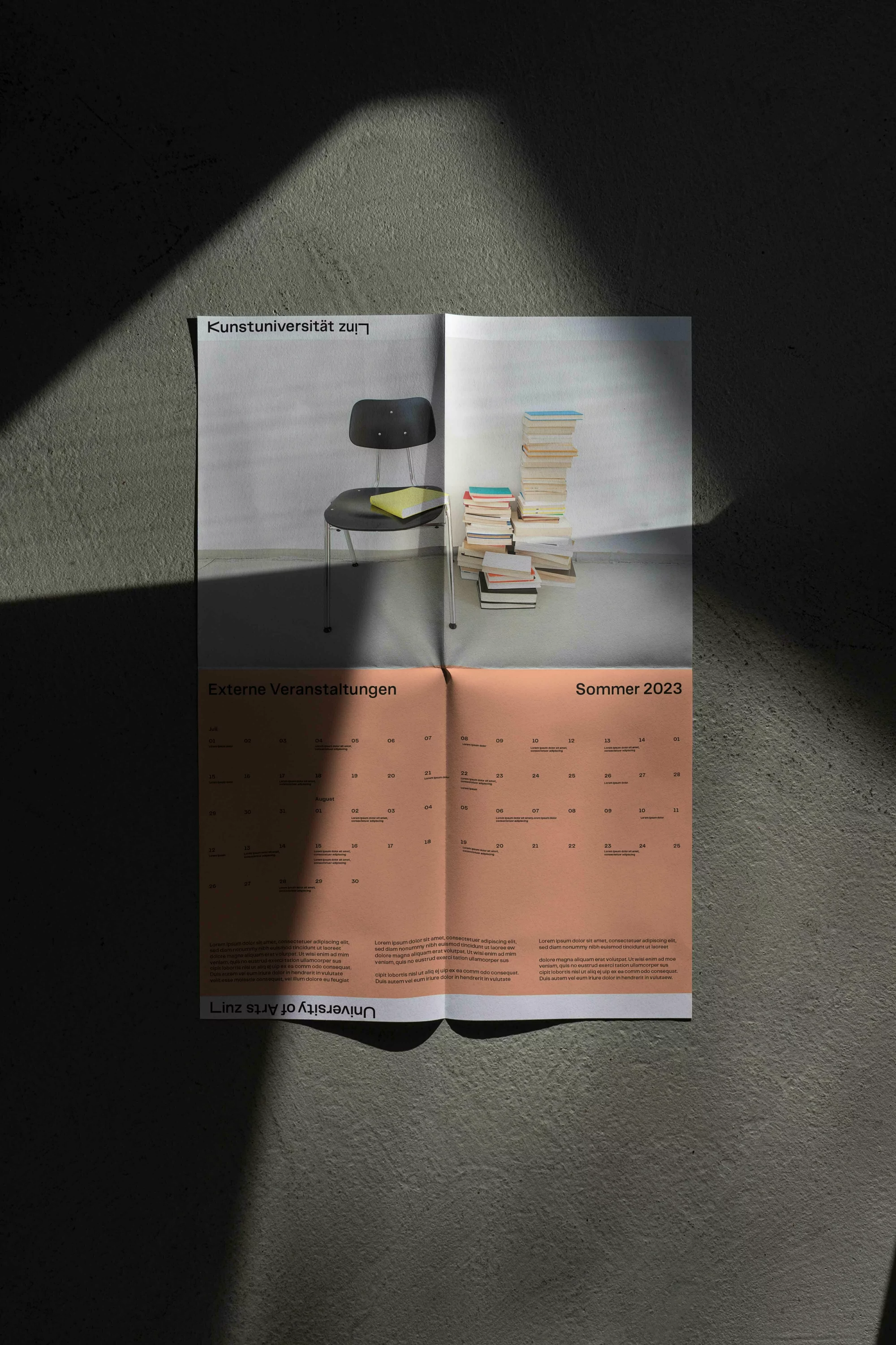 A folded poster is mounted on a gray wall, displaying a chair, books, and a calendar, capturing a blend of design and functionality.