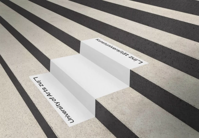 Concrete stairs featuring alternating light and dark treads with institutional typography reading University of Arts Linz