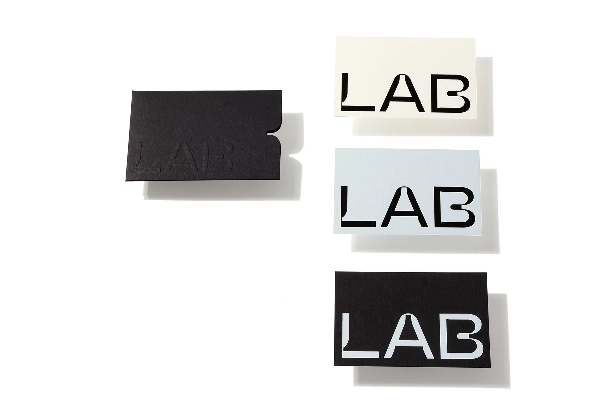 Graphic presentation of black, white, and grey business cards with 'LAB' embossed on each in a studio setting against a white background.