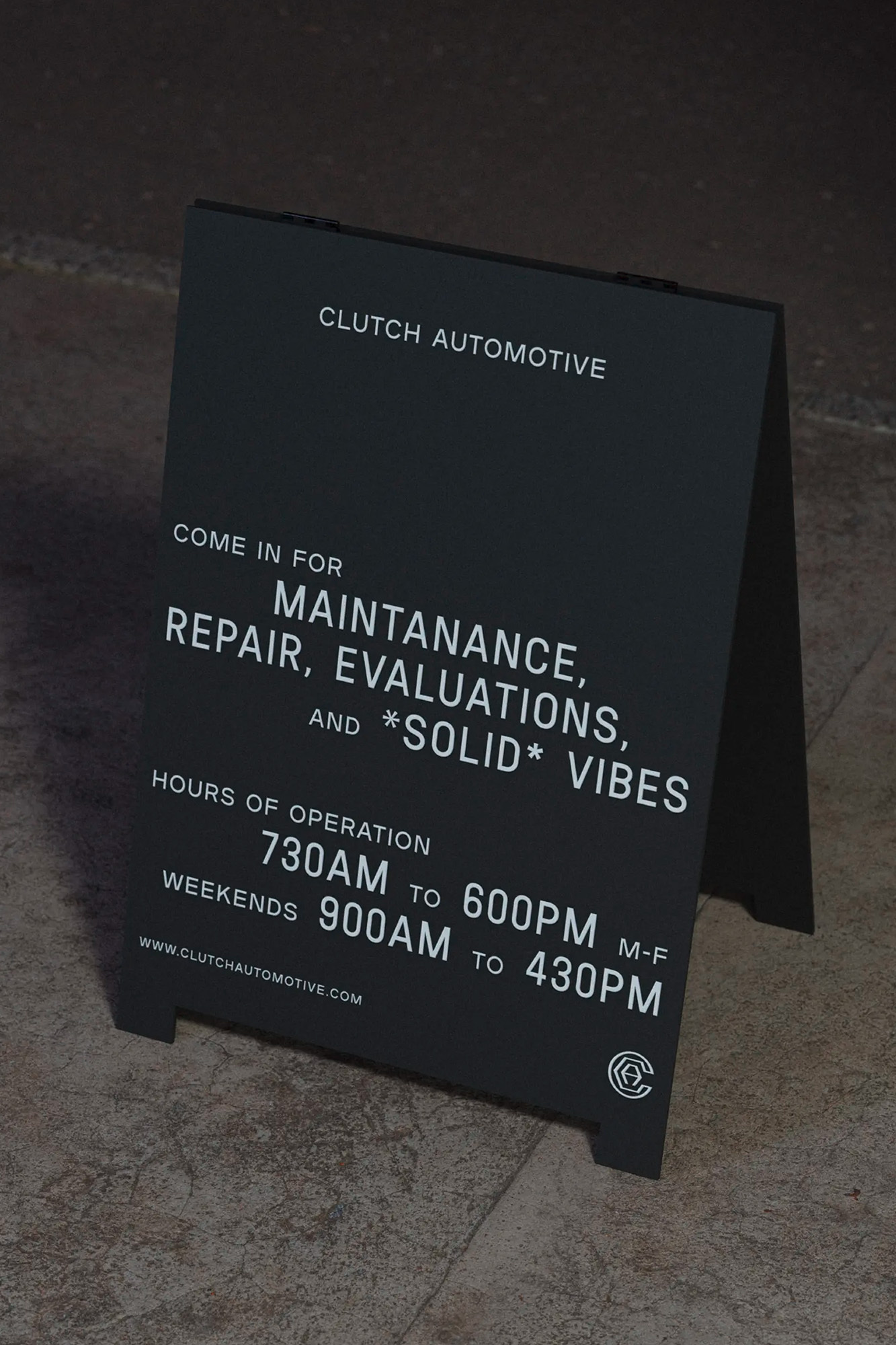 A-frame sign for Clutch Automotive provides hours of operation and advertises maintenance, repair, and solid vibes on a city sidewalk.
