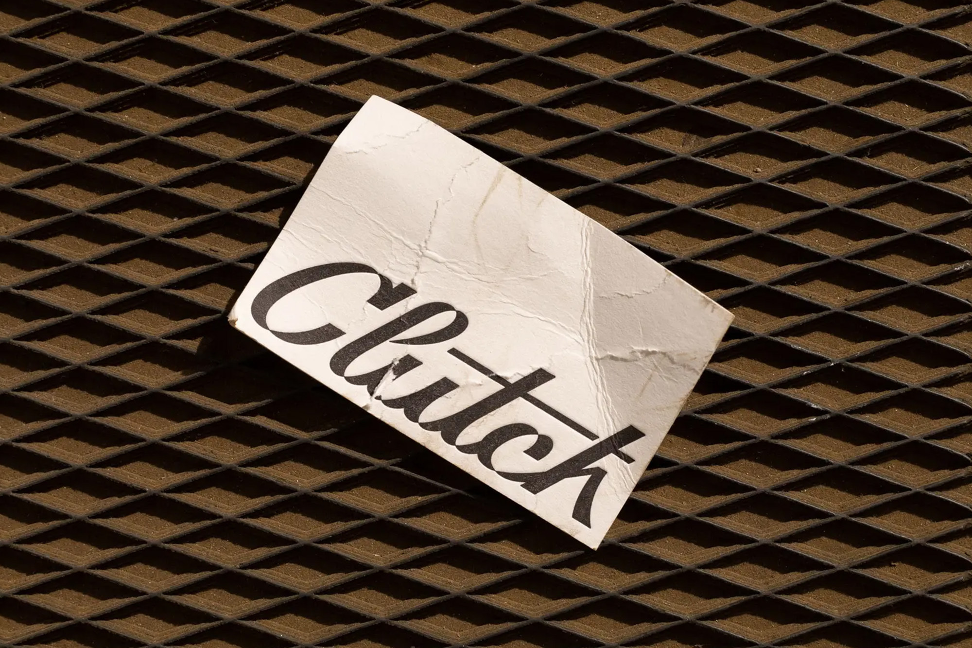 White card with the word Clutch in black text against a dark brown diamond pattern background, angled view.