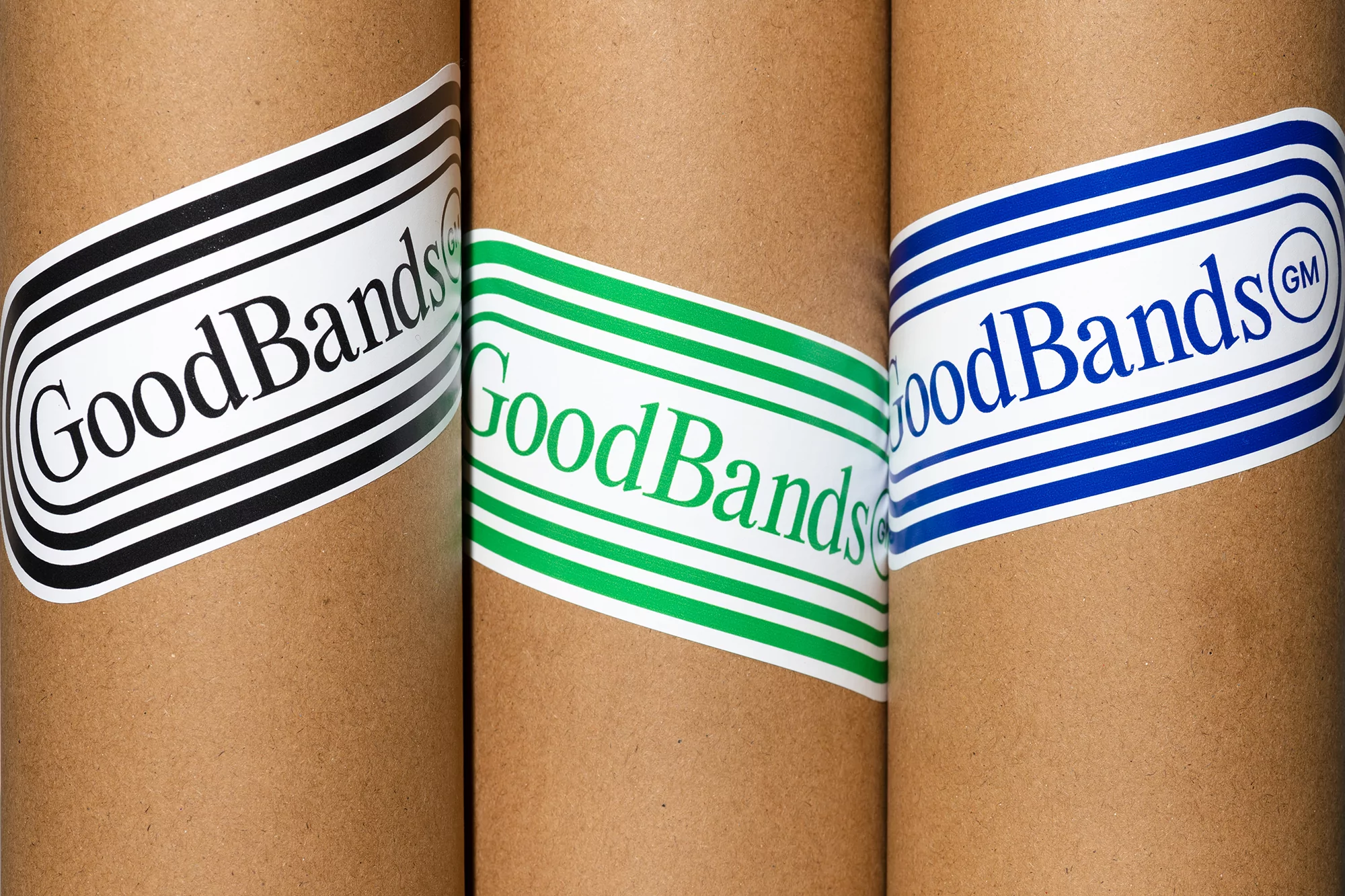 Close-up of three brown cardboard tubes, each featuring a white sticker with the 'GoodBands' logo in black, green, and blue.