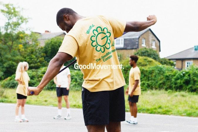 Adult male in a yellow shirt working out with resistance band, other adults standing in the background on a basketball court.