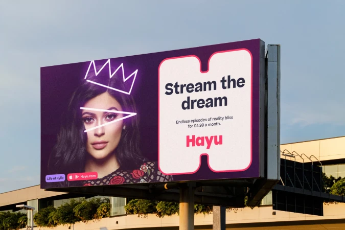 Billboard advertisement featuring a woman with a neon crown and eye decoration, promoting Hayu streaming services against a blue sky.