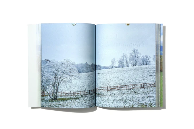 Landscape photograph in an open book shows a snow-covered field with a tree and fence under a light blue sky.