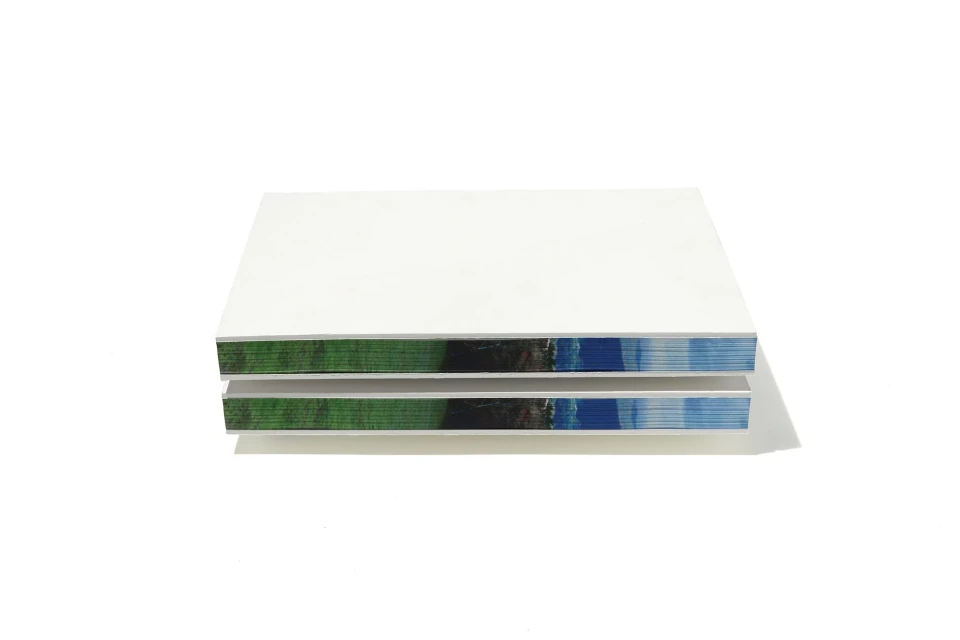 Elevated studio shot of two rectangular volumes stacked with printed edges showing natural landscape colors on a clean white background.