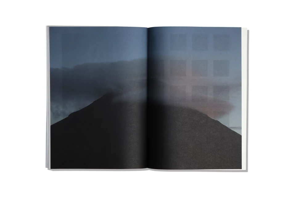 Open book spread displaying a dark landscape with a mountain silhouette and soft, foggy atmosphere, creating an ethereal and moody visual.