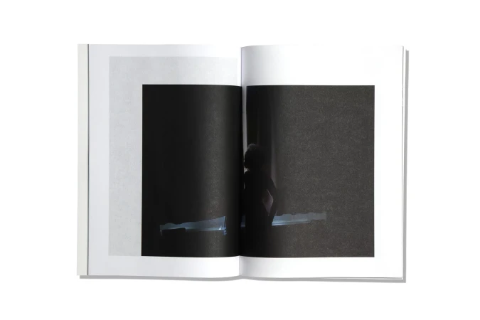 Open book displays a black and white image with a silhouette of a person, positioned on a clean white surface.