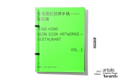 Bright green bound book titled Hong Kong Neon Sign Artworks with a small metallic pen beside it on white background
