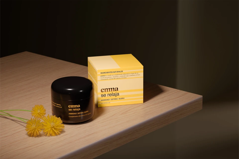Cosmetic product and box on wooden surface with floral accent. Black jar and yellow packaging in soft, natural lighting.
