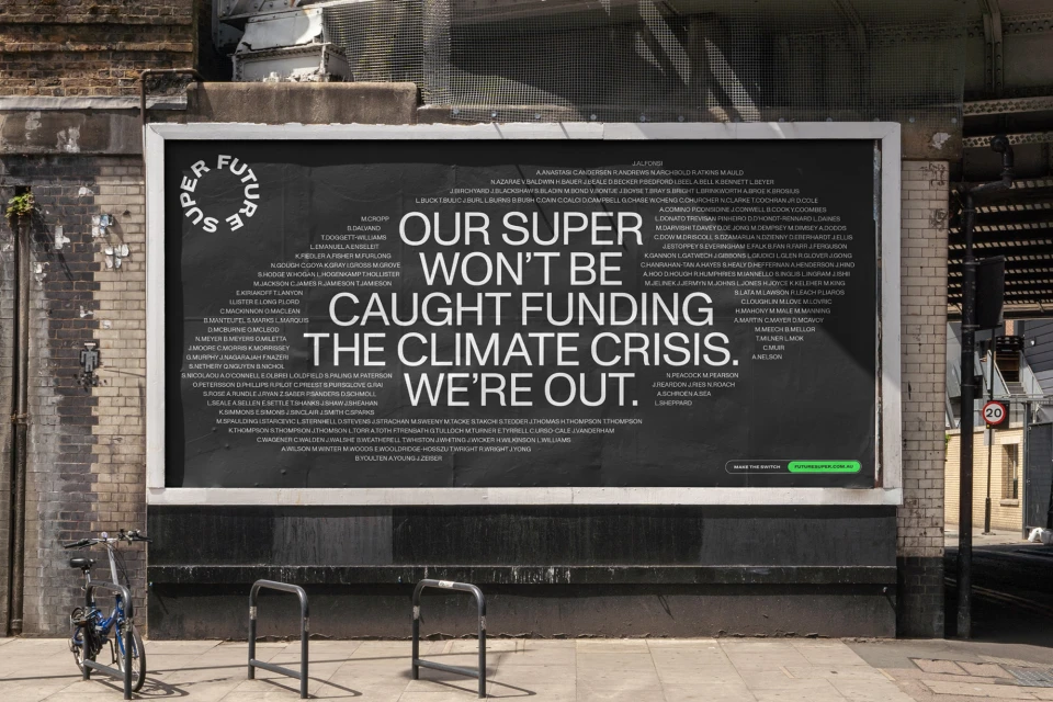 Outdoor billboard on brick wall features large text about climate crisis; bike and metal barrier in front.