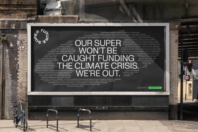 Outdoor billboard on brick wall features large text about climate crisis; bike and metal barrier in front.