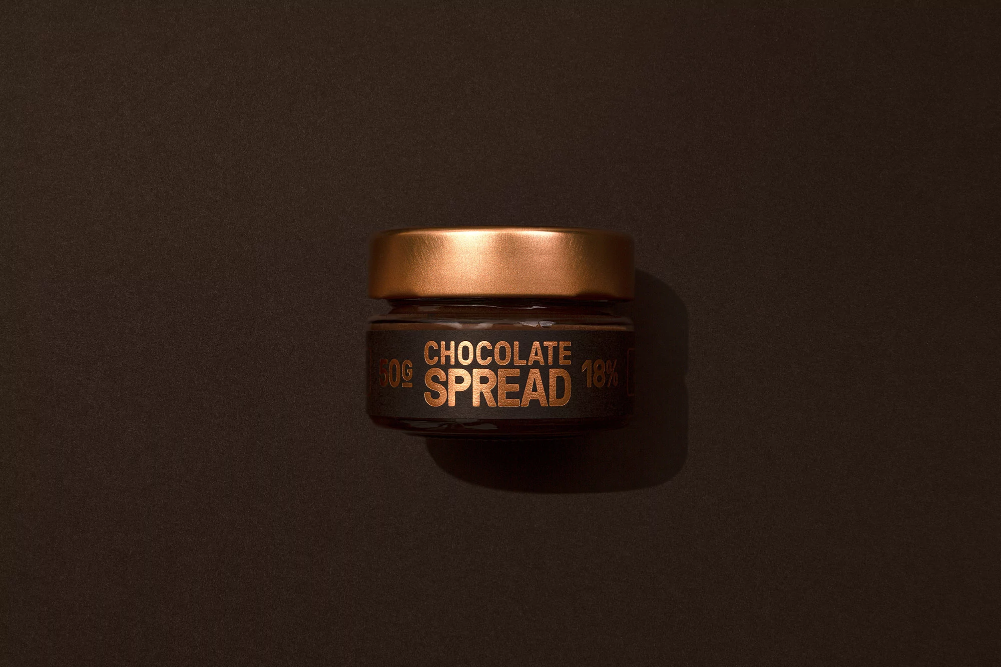 A close-up shot of a jar of chocolate spread with a copper-colored lid on a brown background, featuring product branding and clean presentation.