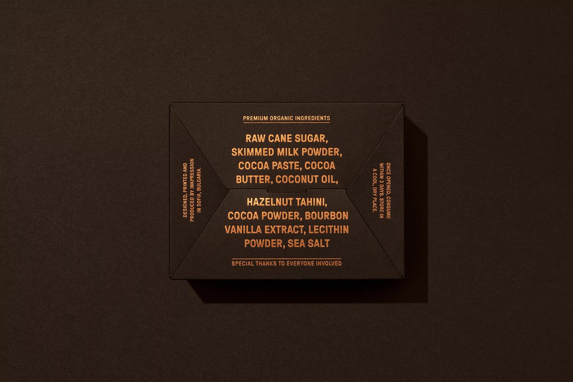 Close-up shot of a dark brown product box with golden text listing premium organic ingredients and design/production details.