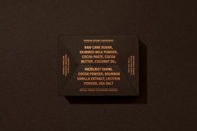 Close-up shot of a dark brown product box with golden text listing premium organic ingredients and design/production details.