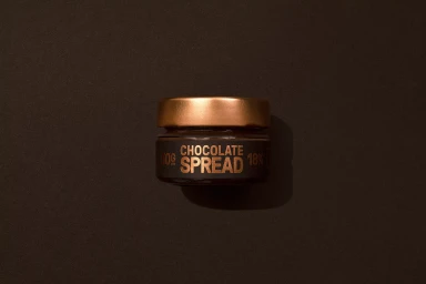 Small glass jar of chocolate spread with a metallic cap centered on a dark brown textured surface