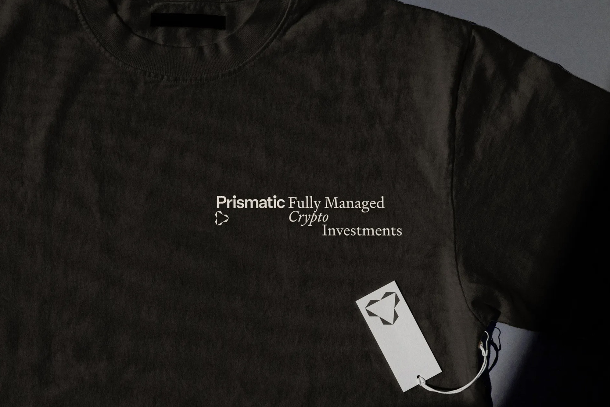 Dark gray T-shirt featuring a logo and text, 'Prismatic Fully Managed Crypto Investments,' complemented by a white tag.