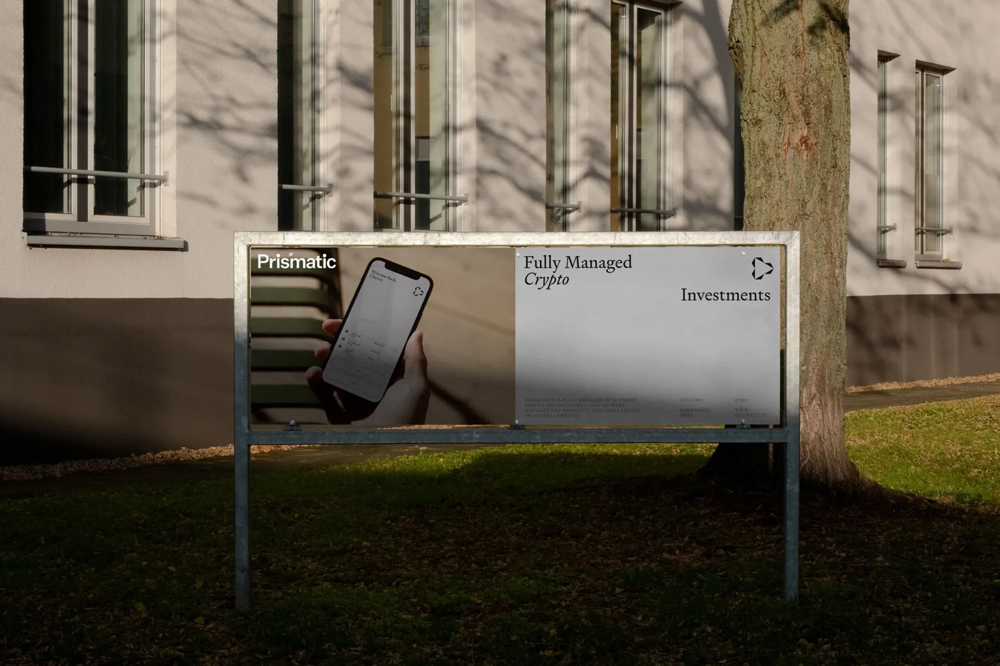 Outdoor advertising sign displaying Prismatic and Fully Managed Crypto Investments against a backdrop of building and tree, set on lawn.