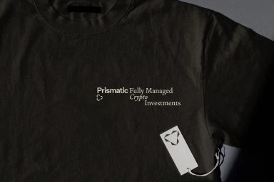Close-up of a dark grey t-shirt featuring Prismatic typography and branding with a white hang tag attached.