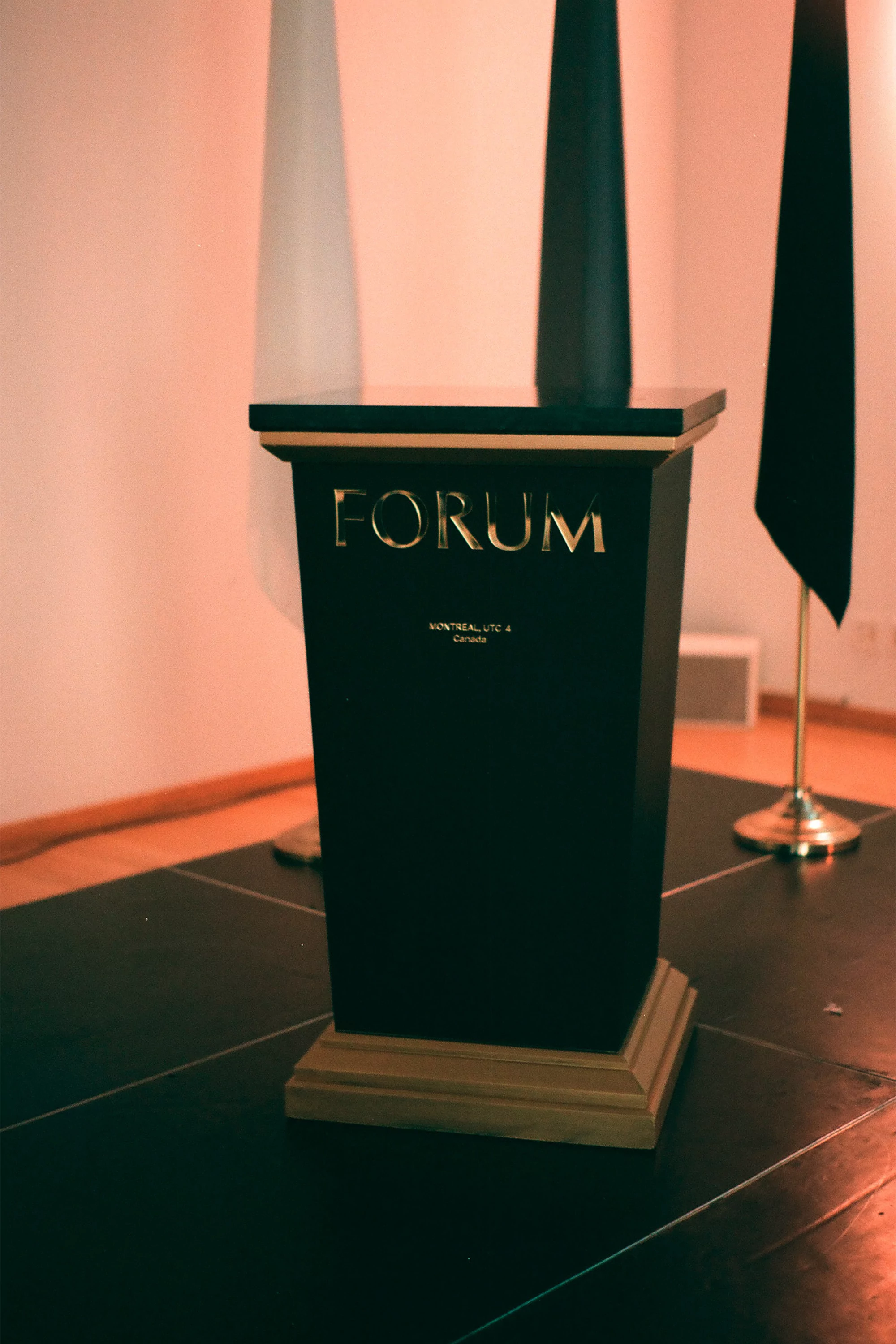 Podium with 'Forum' signage stands indoors with black and white cone-shaped decor and tile flooring in neutral, soft lighting.
