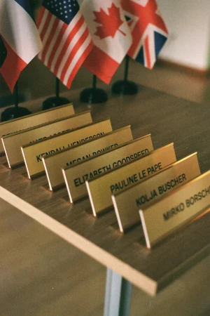 Row of gold desk nameplates on a wooden table beneath small national flags for Casanje brand identity
