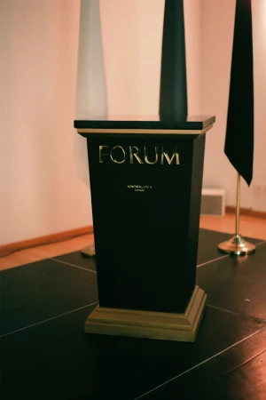 Black pedestal with gold lettering reading FORUM on a dark stage with vertical flags in the background
