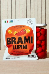 Brami lupini beans pouch and a glass jar filled with red pickled peppers on a textured fabric background