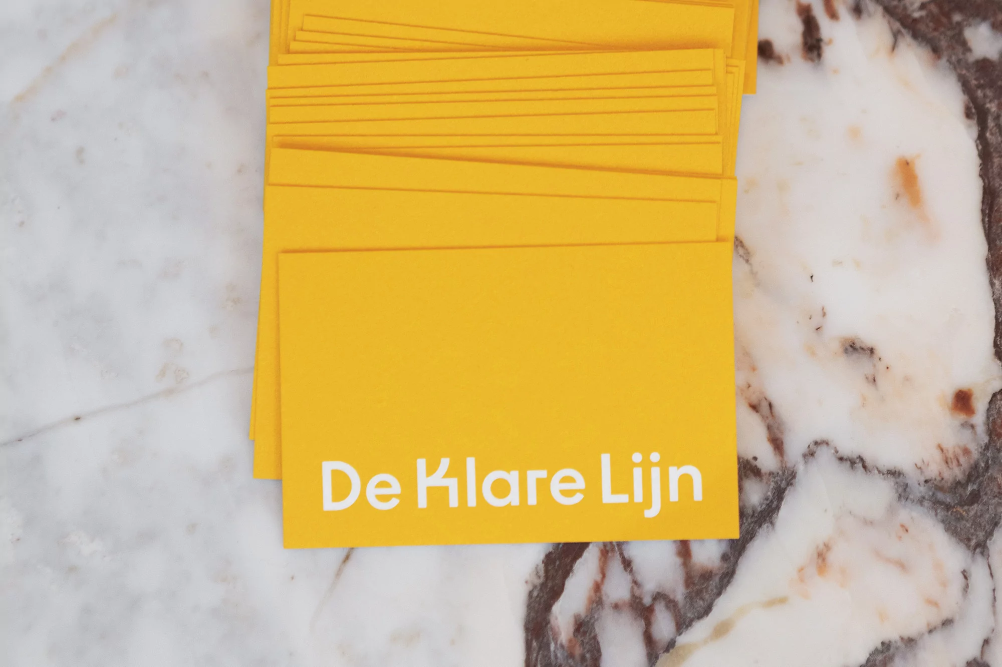 Stack of yellow cards with white text 'De Klare Lijn' on a marble surface, showcasing graphic design and clean, minimalist aesthetic.