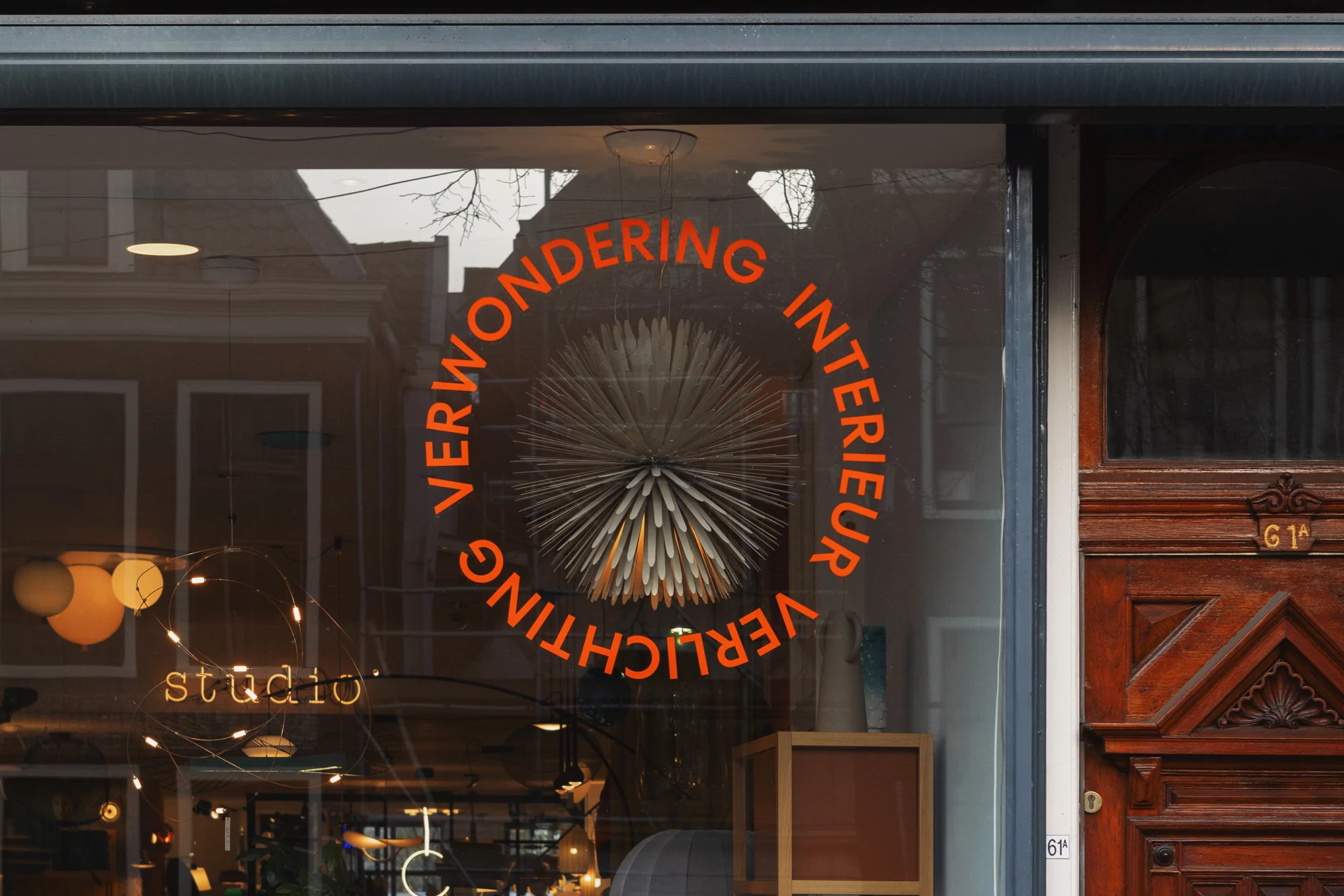 Storefront window with orange text reading 'Verwondering Interieur Verlichting,' featuring a modern light fixture inside.
