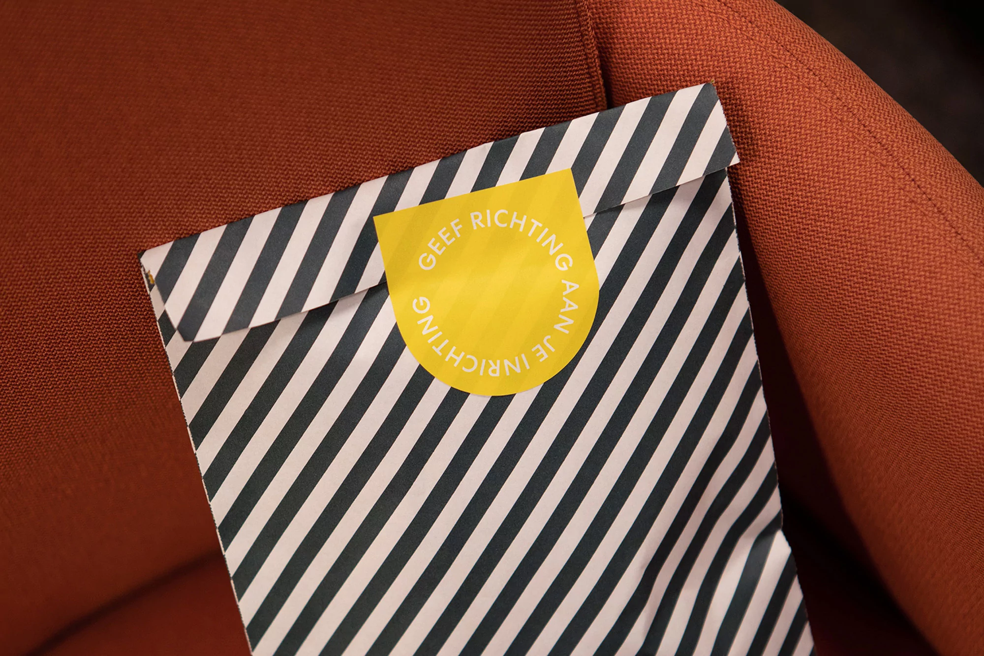 Striped paper envelope with a yellow circular sticker resting on a textured orange armchair surface.