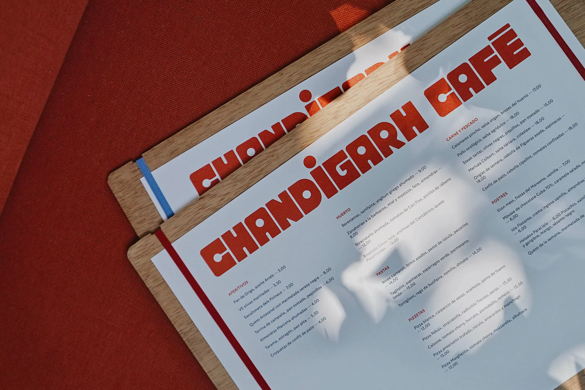 Overhead shot of two restaurant menus on a red surface, featuring the cafe's name in bold letters and lists of food and drink items.