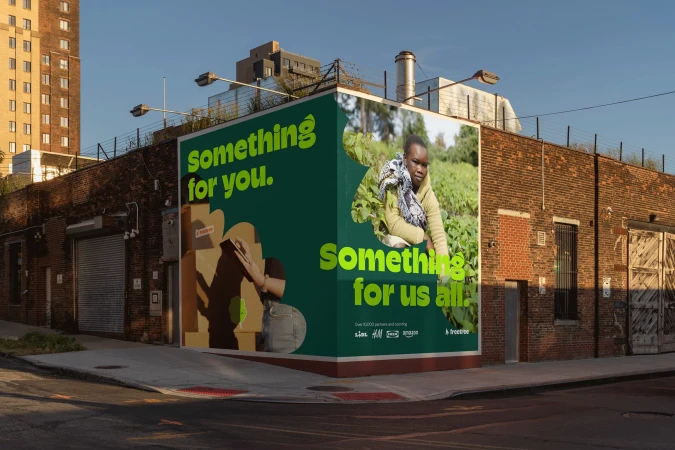 Eye-level outdoor shot of a brick building featuring a large advertisement with an African woman farmer and cardboard box artwork.