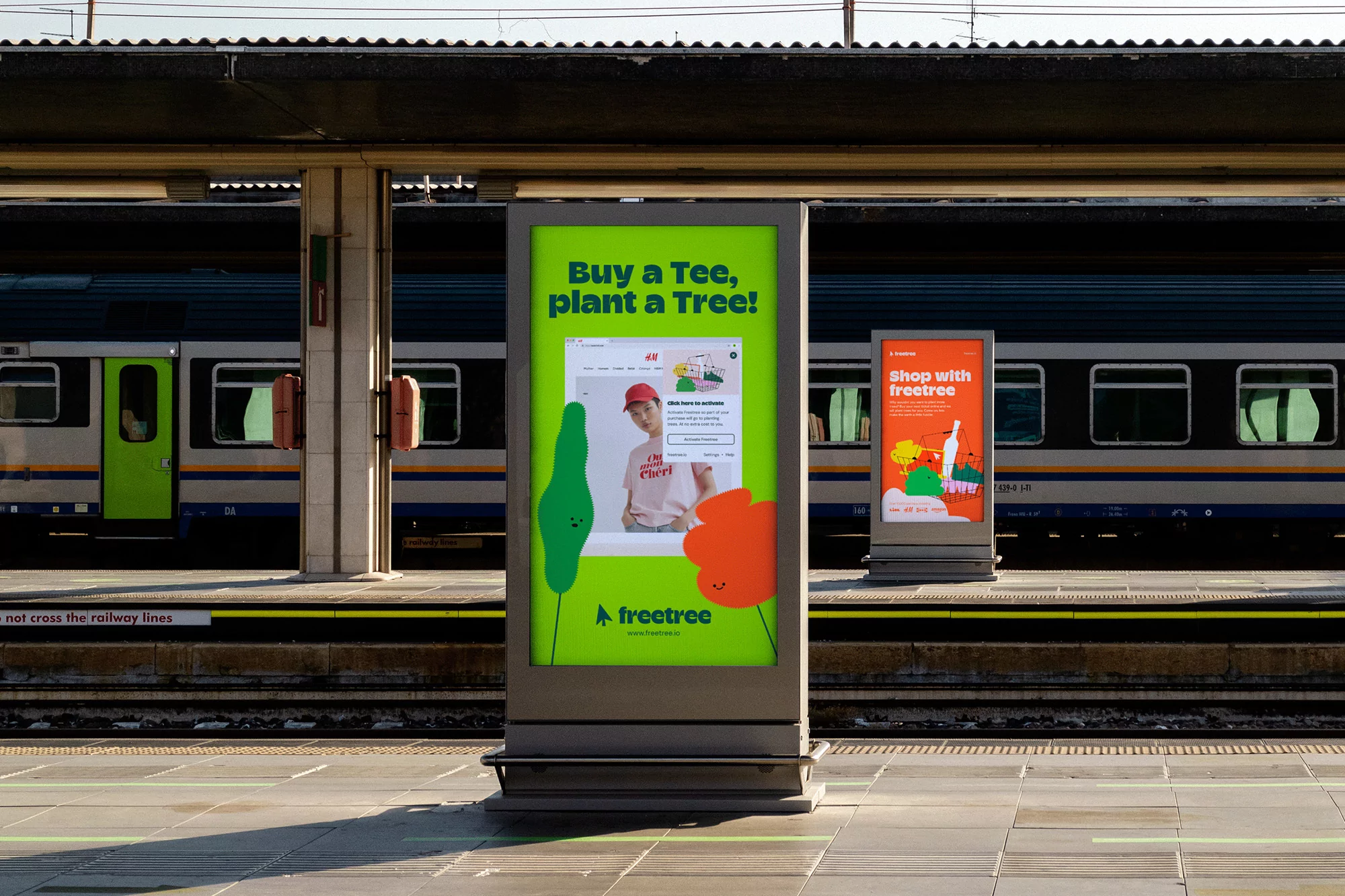 Freetree advertisement on a stand at a train station promoting planting trees for every t-shirt purchased, with a train in the background.