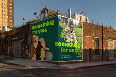 Large green and white outdoor advertising billboard on a brick building corner displaying bold typography and photo of a child