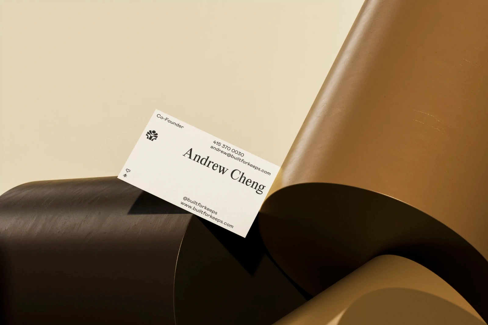 Keeps business card resting among curved brown and cream architectural cylinders in a minimalist studio setup