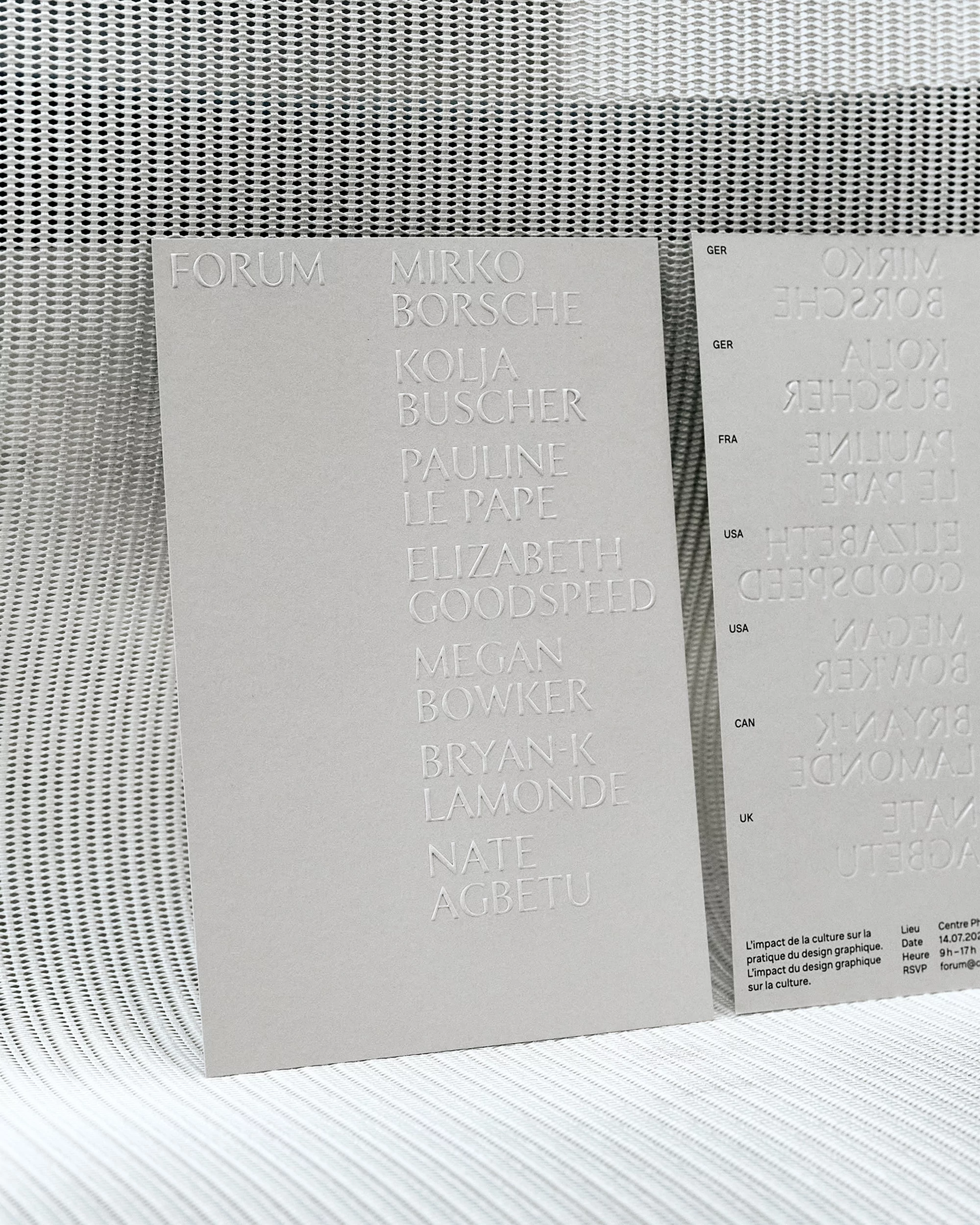 Close-up of two light gray cards displaying embossed text against a textured off-white background, emphasizing minimalist design and material.