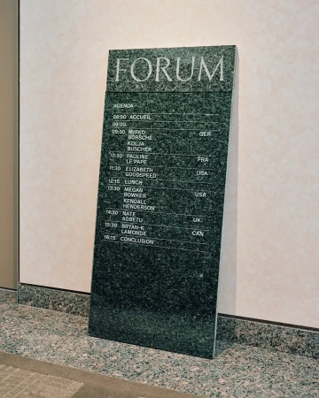 Forum agenda on a marble sign. The agenda includes names such as Mirko Borsche, Kolja Buscher, and Megan Bowker with listed times.