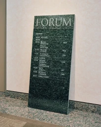 A tall dark green marble monolith sign with engraved white lettering displaying a conference agenda titled FORUM.
