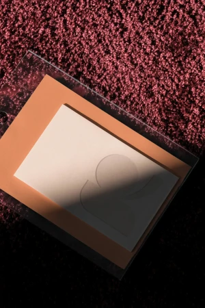 High-angle shot of layered greeting cards, with a textured burgundy carpet backdrop casting shadows and highlights, creating a soft, inviting scene.