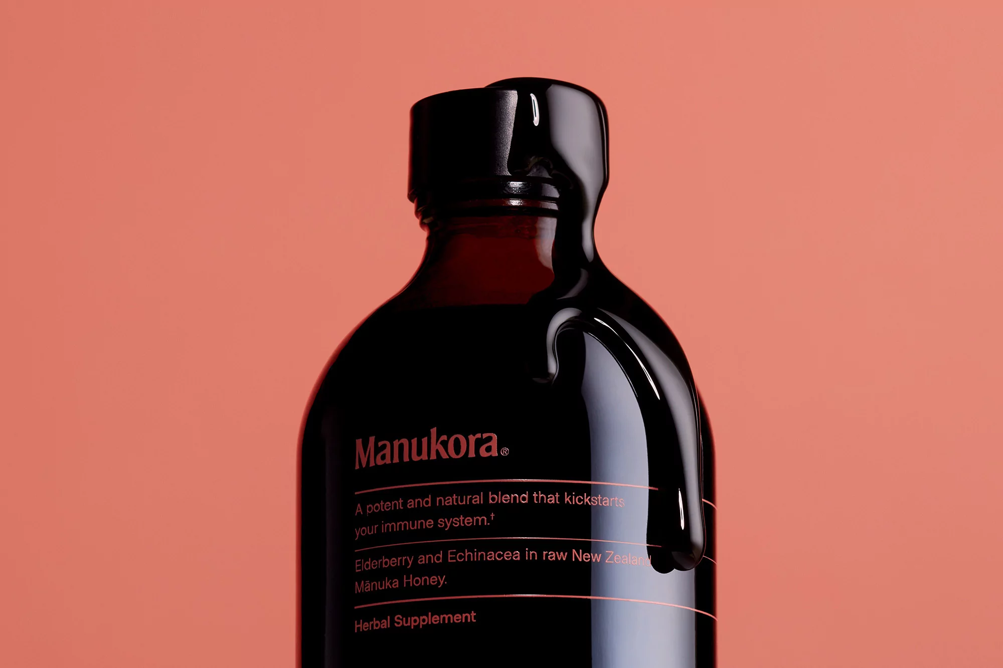 Dark-colored glass bottle of Manukora herbal supplement with black wax seal against a solid light-red background, product shot.