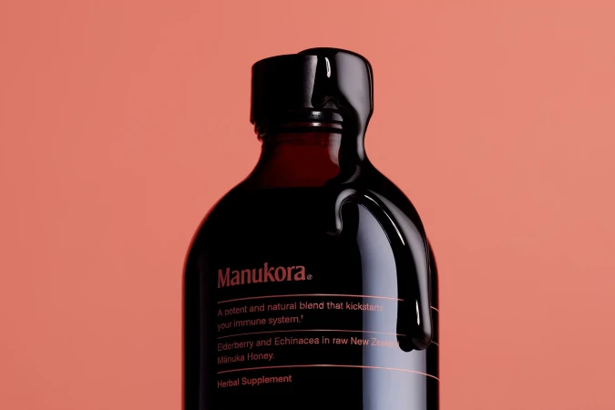 Manukora amber honey bottle with dark liquid dripping over the cap against a terracotta background
