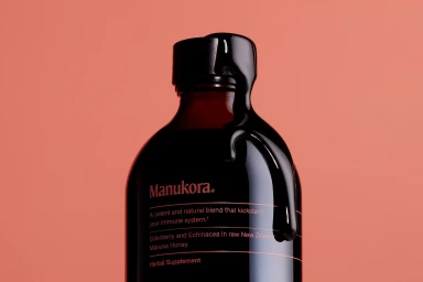 Manukora amber honey bottle with dark liquid dripping over the cap against a terracotta background