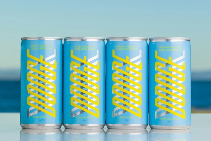 Four cans of DUDEK drink line up, showcasing light blue cans with yellow and silver geometric branding against a soft blue gradient backdrop.