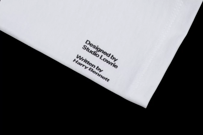Close-up of a white cloth with black text that reads 'Designed by Studio Lowrie, Written by Harry Bennett' against a black background.