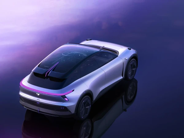 Sleek silver electric car with a panoramic glass roof is showcased in a studio setting with a reflective surface and a purple gradient backdrop.
