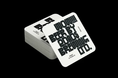 Stack of square white cardboard coasters featuring bold black typography for 2DADS against a solid black background.