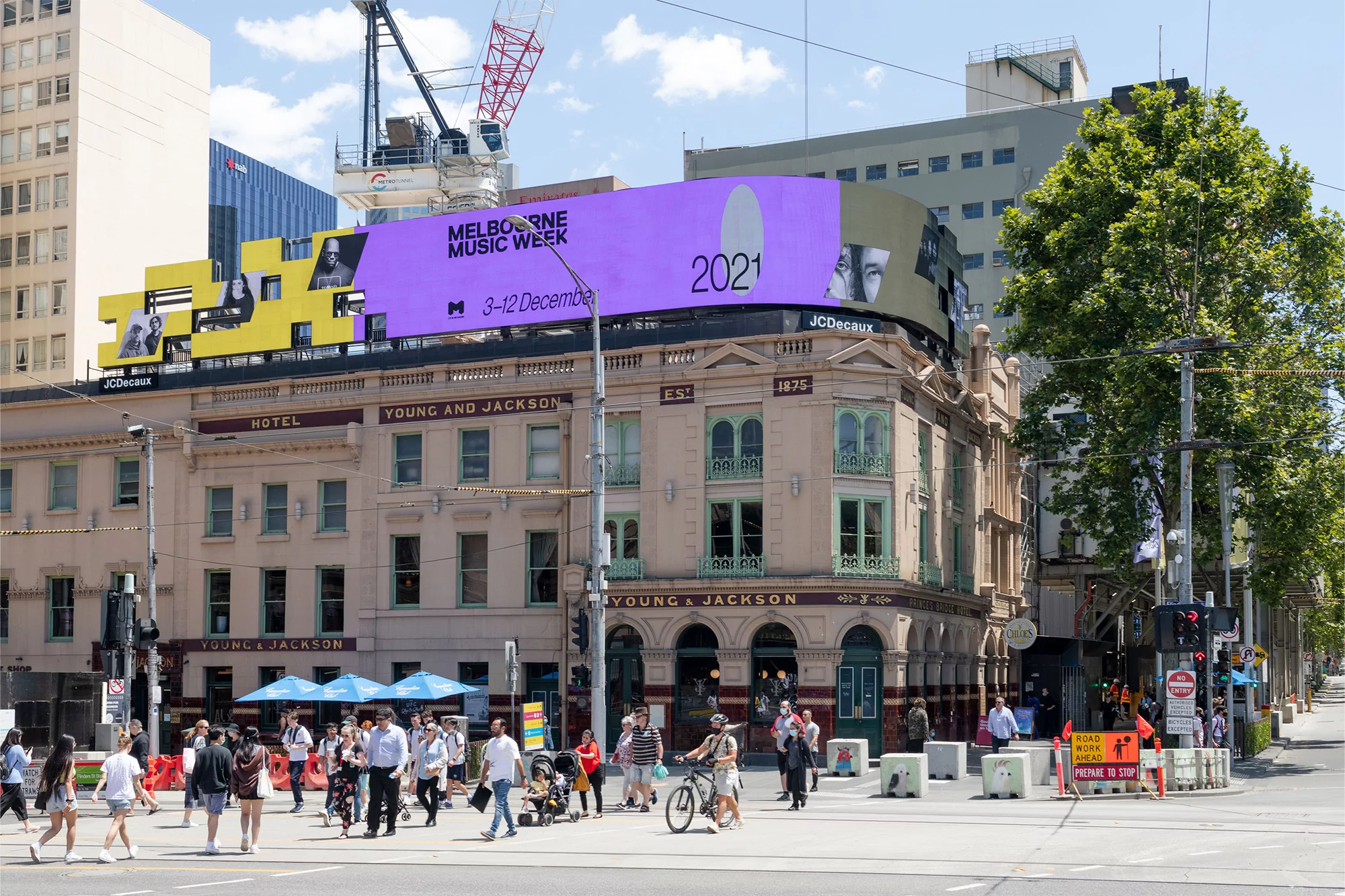 Melbourne, Australia street scene with a pedestrian crossing and a vintage hotel building displaying an advertisement for Music Week.